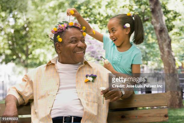 african granddaughter decorating grandfather's head with flowers - extended family outdoors spring stock pictures, royalty-free photos & images