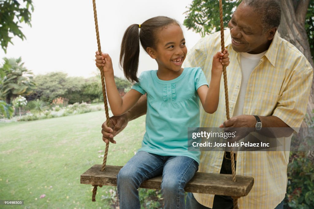 African grandfather pushing granddaughter on swing