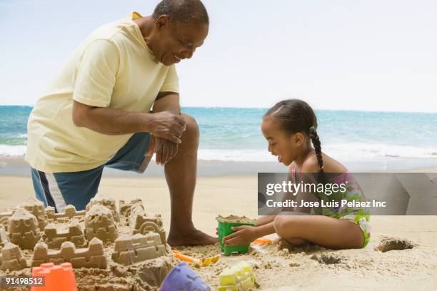 african grandfather and granddaughter building sand castle - kind sandburg stock-fotos und bilder