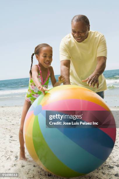 african grandfather and granddaughter playing on beach with large ball - summer press day ストックフォトと画像