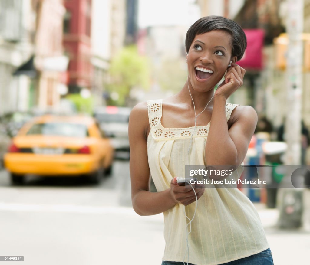 African woman on urban street listening to headphones