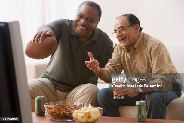 men watching football game in living room with snacks - american football game stockfoto's en -beelden