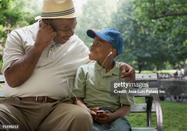 african grandfather and grandson sharing headphones on park bench - boy ipod stock pictures, royalty-free photos & images