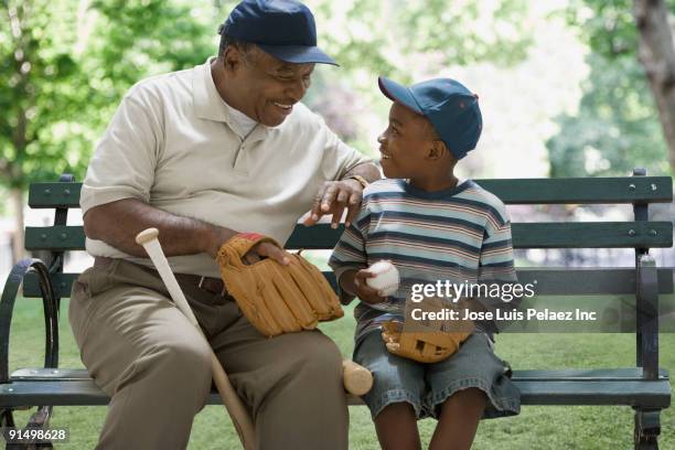 african grandfather and grandson holding baseball equipment on park bench - west new york new jersey stock-fotos und bilder