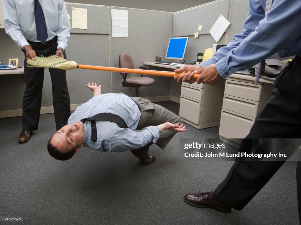 Businessmen playing limbo with broom in office