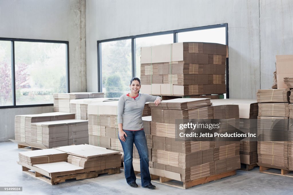 Mixed race woman leaning on flattened boxes in warehouse