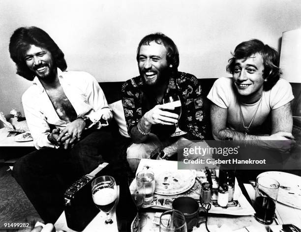 The Bee Gees posed sitting at a table in Amsterdam in 1975. L-R Barry Gibb, Maurice Gibb, Robin Gibb