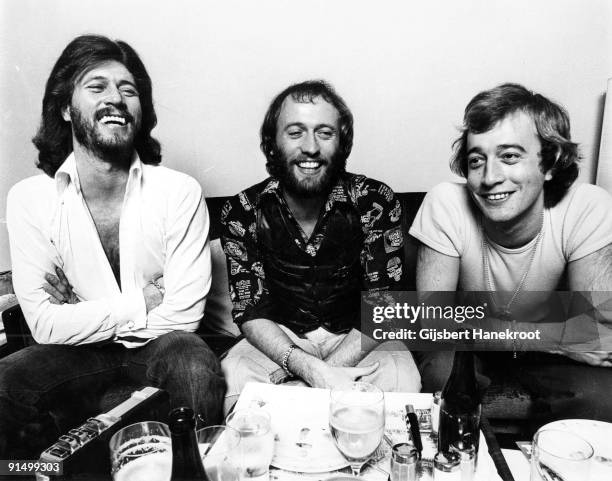 The Bee Gees posed sitting at a table in Amsterdam in 1975. L-R Barry Gibb, Maurice Gibb, Robin Gibb