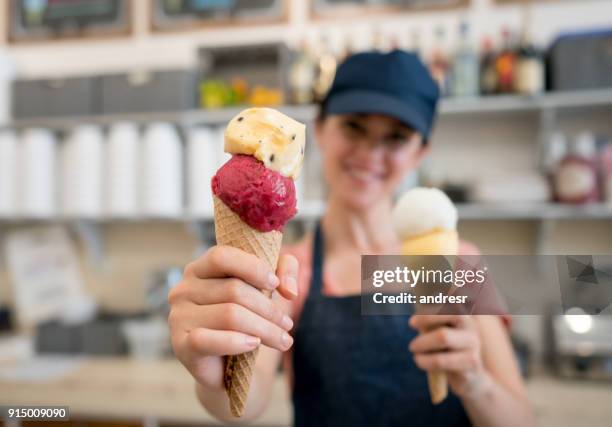 female employee at an ice cream parlor holding to ice cream cones looking at camera smiling - ice cream parlour stock pictures, royalty-free photos & images