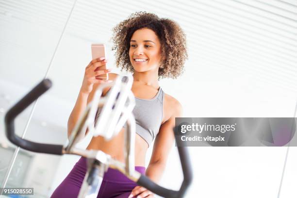 woman on a stationary bike at the gym using smart phone - peloton app stock pictures, royalty-free photos & images