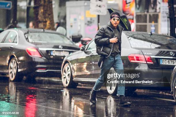 Guest wears a bandanna, a black puffer coat, blue cropped jeans, black shoes, under the rain, outside Paul Smith, during Paris Fashion Week -...