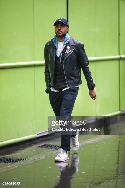 Guest wears a cap, a black leather jacket, a black puffer coat, black jeans, white sneakers, under the rain, outside Paul Smith, during Paris Fashion...