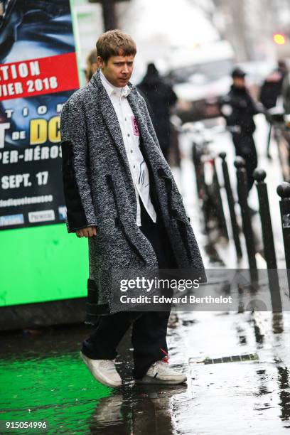 Guest wears a white shirt, a long coat, black pants, shoes, under the rain, outside Paul Smith, during Paris Fashion Week - Menswear Fall Winter...