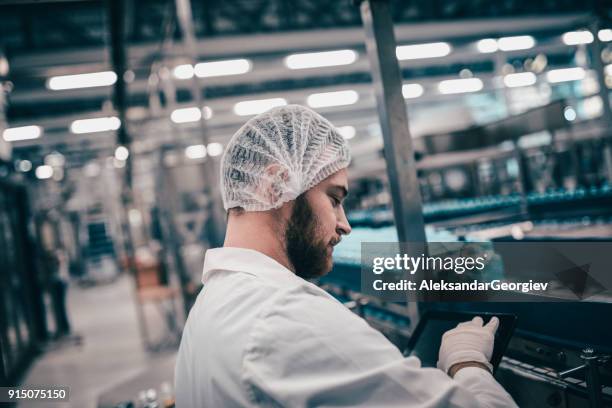factory engineer with hair net operating machine with digital tablet - rede de cabelo imagens e fotografias de stock
