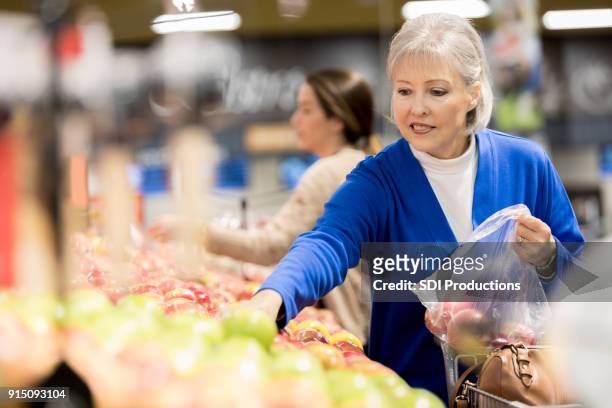 confident woman picks out apples in grocery store - picking up groceries stock pictures, royalty-free photos & images