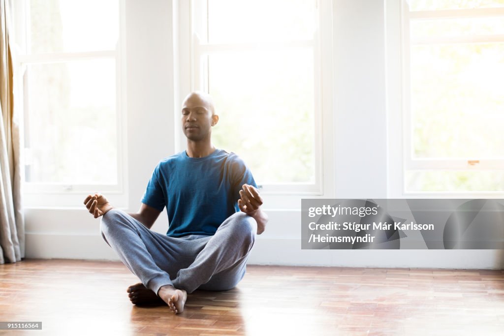 Man practicing yoga in lotus position at home