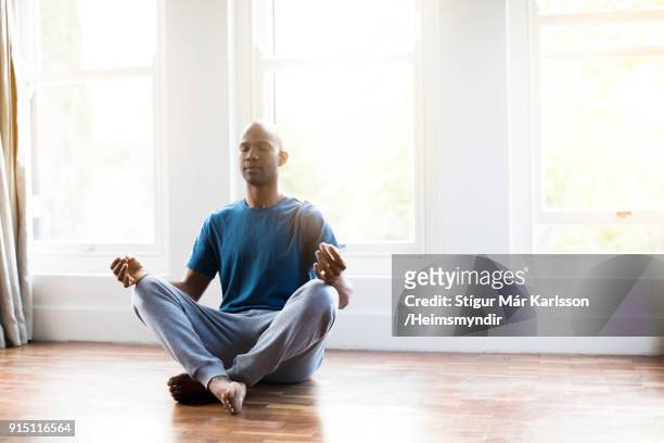 man practicing yoga in lotus position at home - cross legged stock pictures, royalty-free photos & images