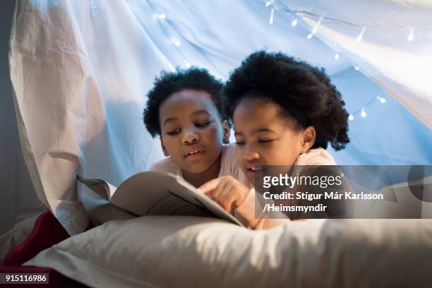 Girls reading story book while lying on bed