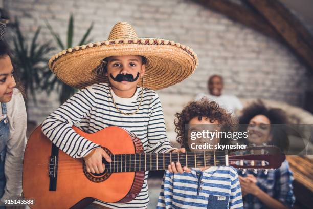 little mariachi boy playing a guitar to his family at home. - sombrero stock pictures, royalty-free photos & images