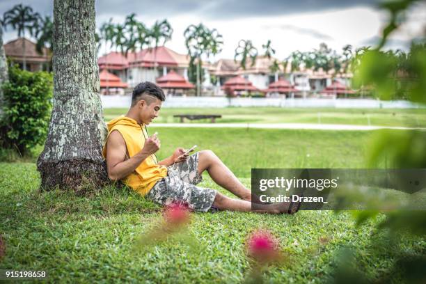 young thai man hears list of his favorite games outside smartphone home - playlist with the a list stock pictures, royalty-free photos & images