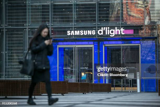 Woman uses her smartphone as she walks past a sign for the Samsung Electronics Co. D'light flagship store at the company's Seocho office building in...