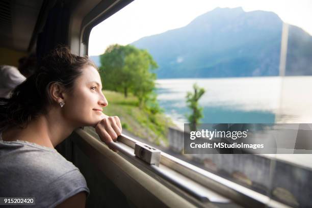 smiling woman looking at the view from train - train window stock pictures, royalty-free photos & images