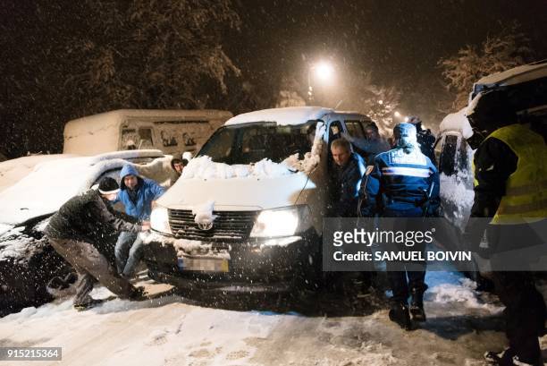 People try to move a car, as vehicles are stranded by the snow on a road near Bievres, southwest of Paris, early February 7 after heavy overnight...