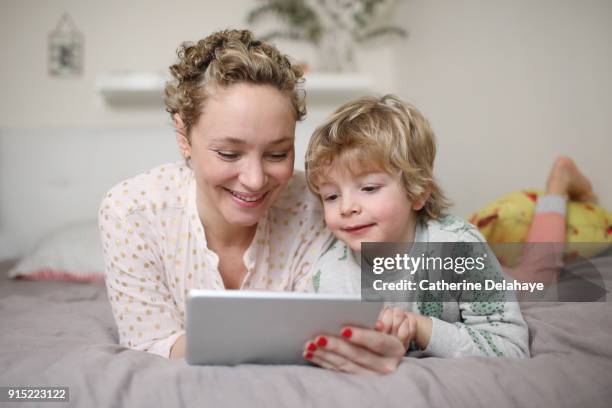 a mum and his son watching a tablet - boy in pajamas and mom on tablet stock-fotos und bilder
