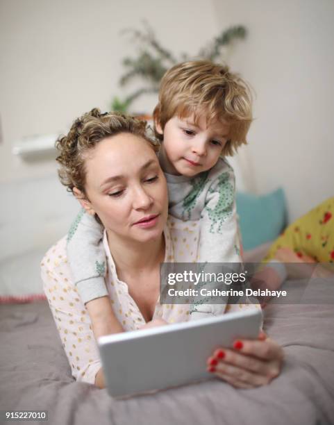 a mum and his son watching a tablet - boy in pajamas and mom on tablet stock-fotos und bilder