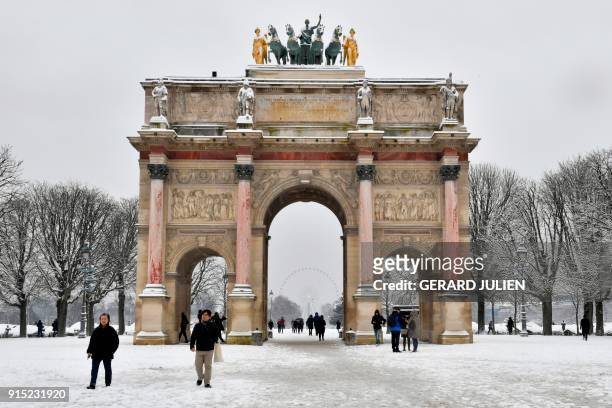 People pass by the Arc de Triomphe du Caroussel as they walk through the snow covered Tuileries garden on February 7, 2018 in Paris. Exceptionally...