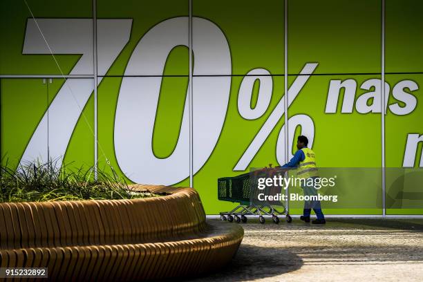 Worker collects shopping carts outside an advertisement for 70 percent discounts at the Dolce Vita Tejo shopping mall, operated by AXA Real Estate...