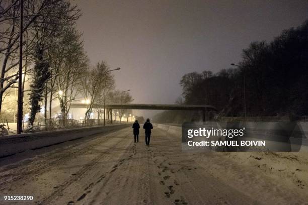 People walk on the deserted and snow-covered N118 main road near Velizy-Villacoublay overnight on February 6 after its closure following heavy...