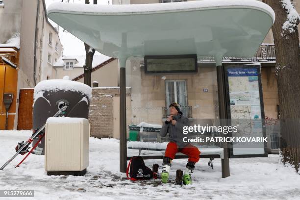 Man prepares his skis in a bus shelter on the snow-covered Montmartre hill on February 7, 2018 in Paris. Exceptionally heavy snowfall brought public...
