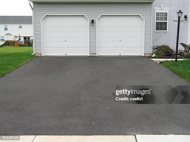 a double garage with white doors at the end of a driveway - asphalt stockfoto's en -beelden