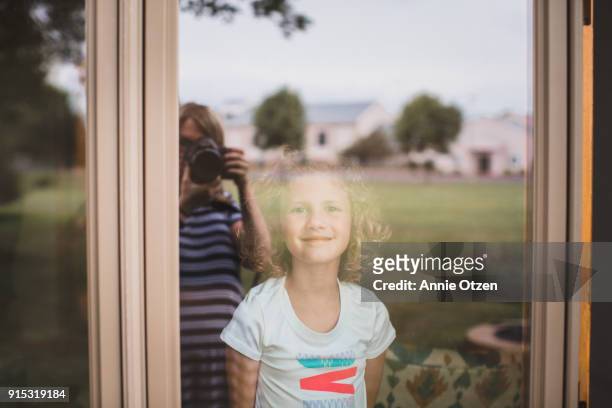 Little Girl Looks Through a window at a photographer