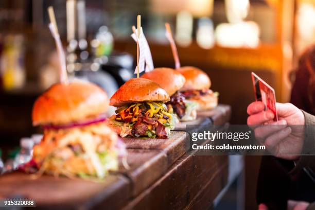 close up of man paying for fresh flame grilled burgers displayed in a row at food market using credit or debit card - pattie sellers stock pictures, royalty-free photos & images