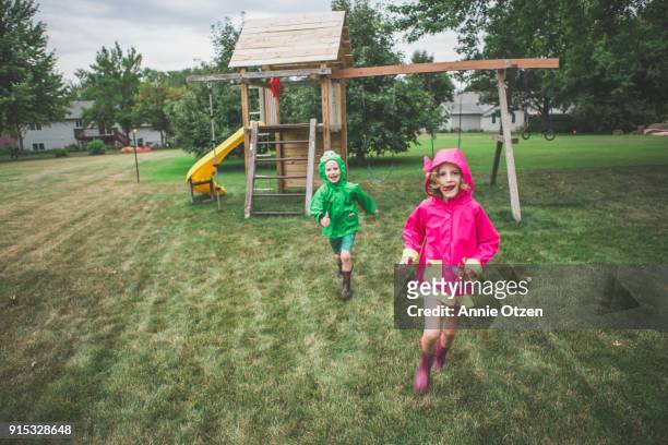 kids running across a backyard in raincoats - schaukel regen stock-fotos und bilder