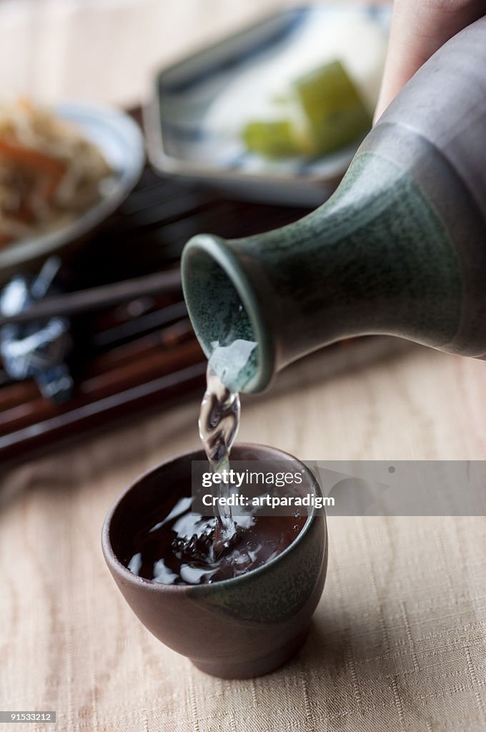 Filling a cup with Japanese sake, and side dishes