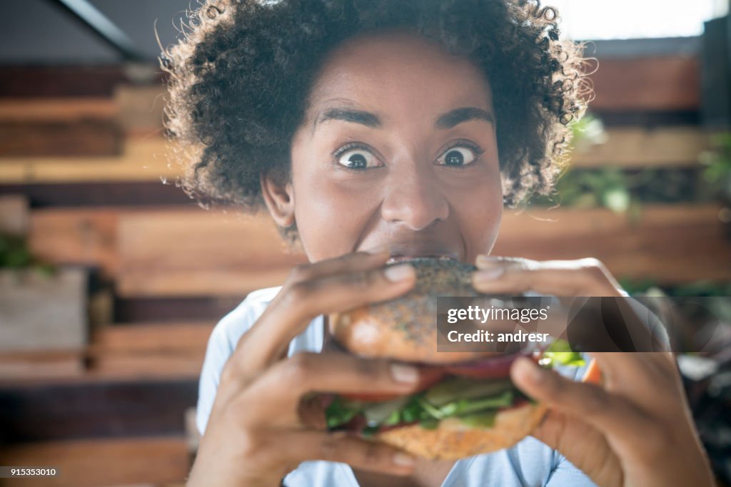 Expressiva mulher afro-americana comendo um hambúrguer vegetariano delicioso