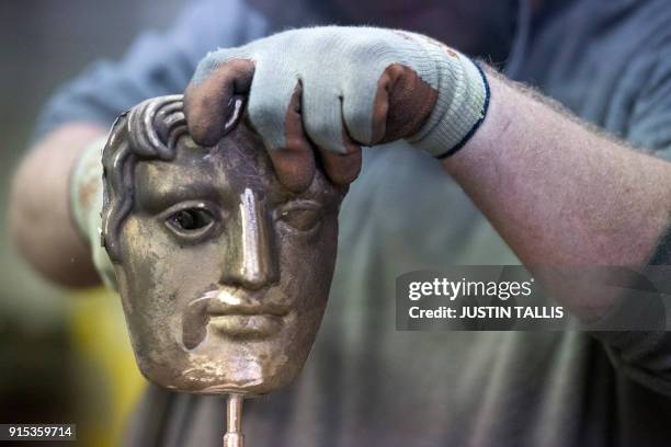 Worker fettles a BAFTA mask during a photo call at the New Pro Foundries, west of London, on February 7, 2018 ahead of the British Academy Film...