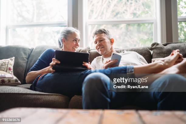 coppia matura rilassante con tablet e smartphone - comodità foto e immagini stock
