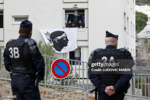 Riot policemen watch as residents display a Corsican flag in the window of a building near the Alb'Oru cultural centre, where the French President...