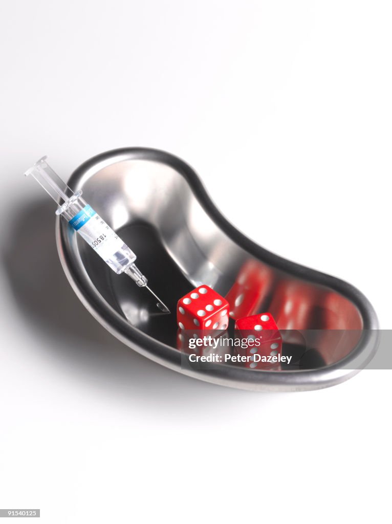 Flu vaccine syringe in kidney dish with dice.