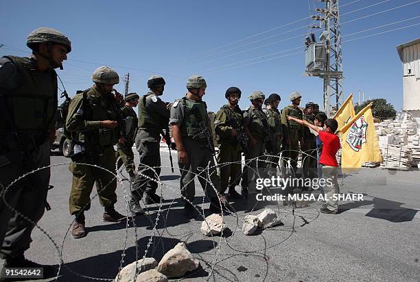 Palestinian boys wave the Fatah party flag in front of Israeli soldiers standing guard during a protest against Israel's controversial separation...