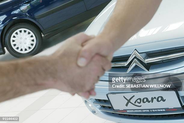 Customer shakes hands with a car dealer in front of Xsara limousine on July 15 at Citroën story in Leipzig. AFP PHOTO/DDP/SEBASTIAN WILLNOV