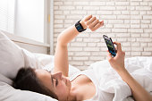 Woman On Bed Synchronizing Smart Watch With Cell Phone