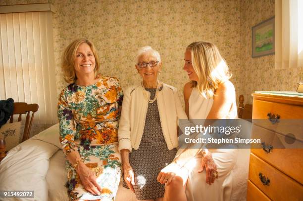 portrait of blonde bride sitting with mom and great grandmother on bed on wedding day - kitchen dresser stock pictures, royalty-free photos & images