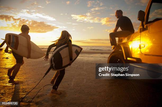 young surfers run to the ocean while their dad watches - californie surf stock pictures, royalty-free photos & images