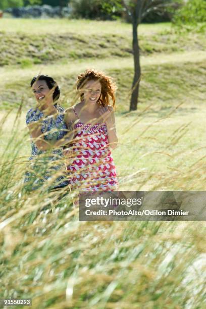 two young women laughing together outdoors, tall grass in foreground - joined at hip stock pictures, royalty-free photos & images