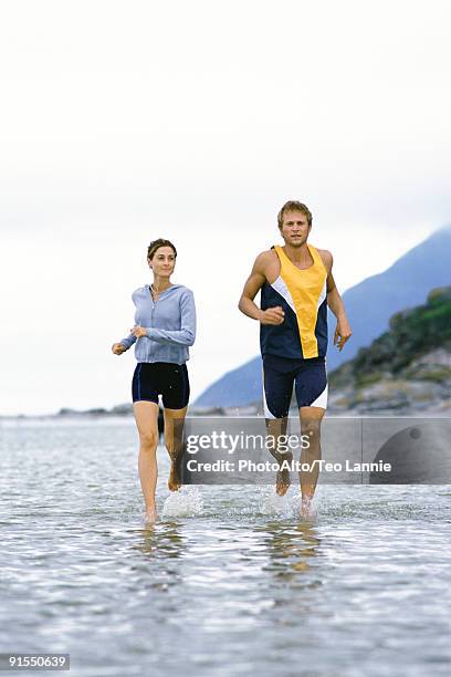 young couple running together through shallow  water near shore - peu profond photos et images de collection